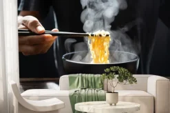 Fototapeta: Hand uses chopsticks to pickup tasty noodles with steam and smoke