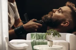 Fototapeta: Young bearded man getting beard haircut by hairdresser
