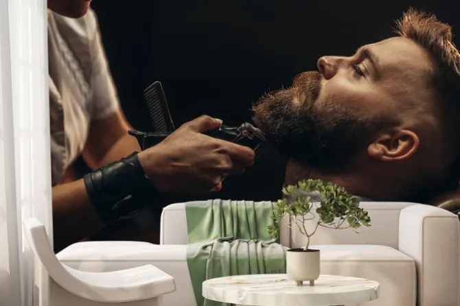 Fototapeta: Young bearded man getting beard haircut by hairdresser
